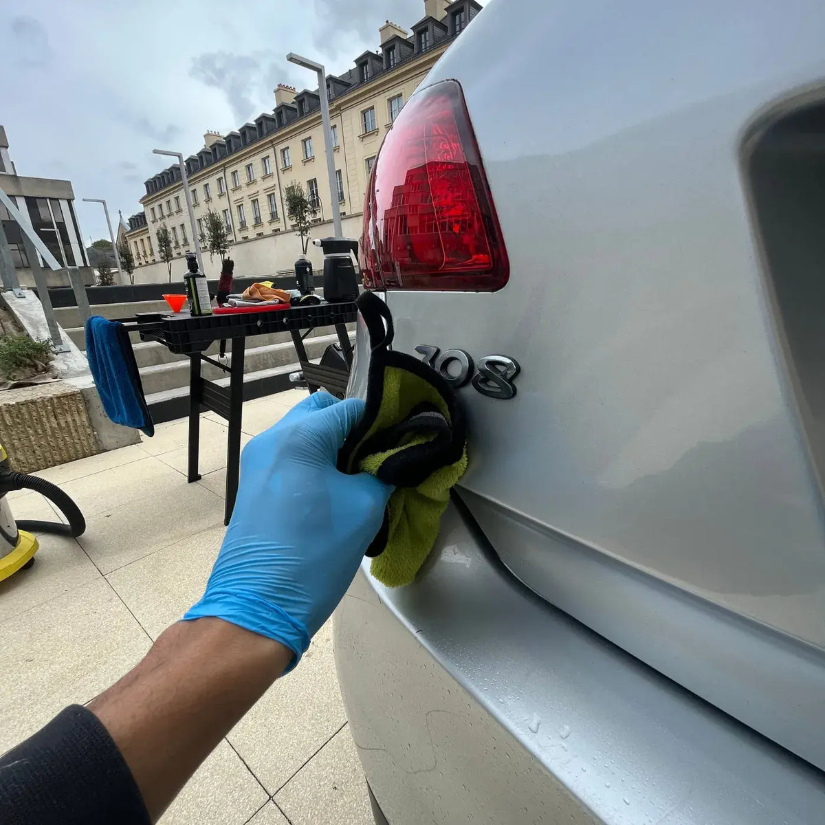 Finition de la carrosserie arrière d’une voiture blanche à Saint-Ouen-l’Aumône, avec essuyage autour du badge 308 à la microfibre.