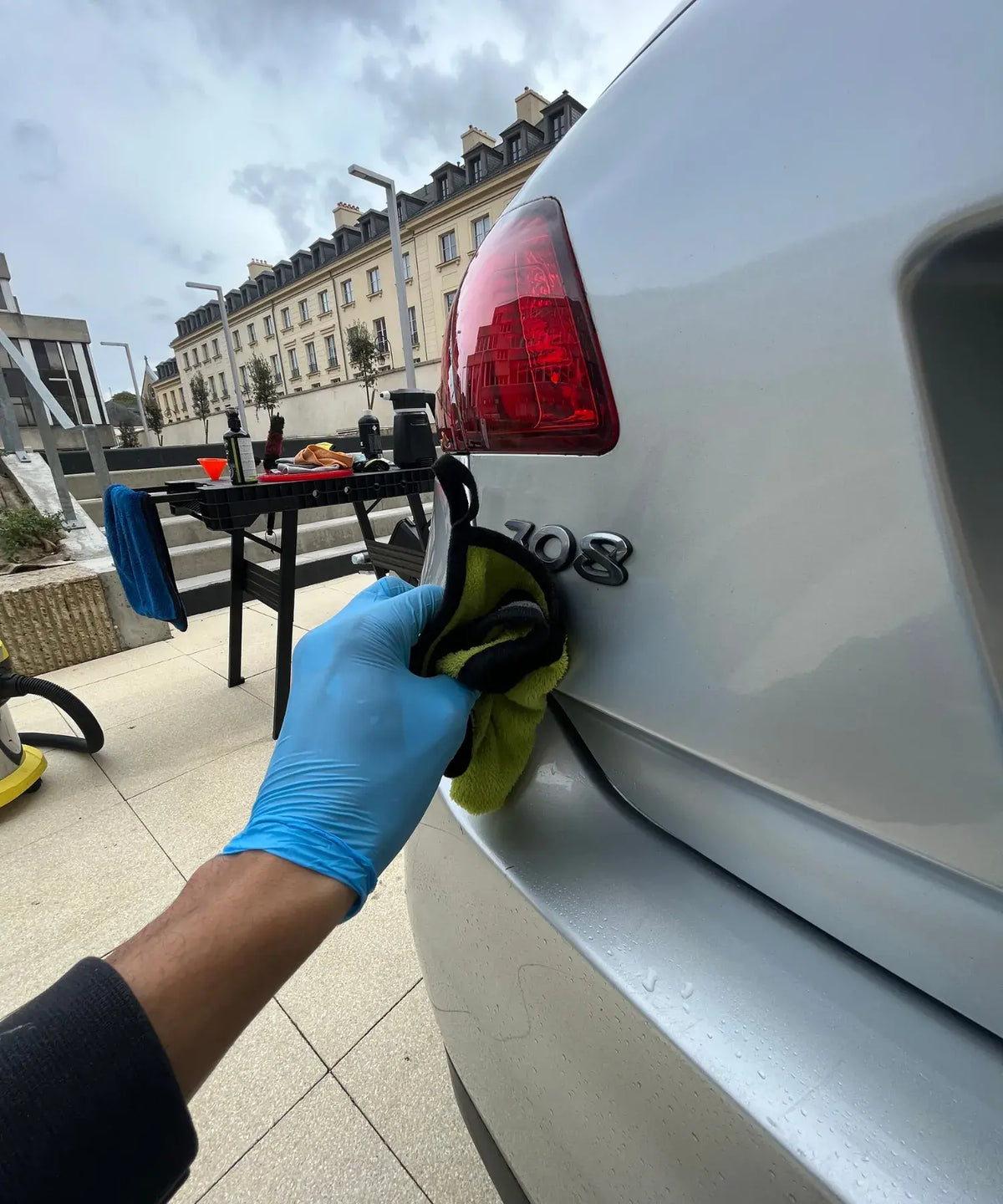 Nettoyage de la carrosserie d’une voiture blanche à Bezons, essuyage du coffre avec une microfibre.